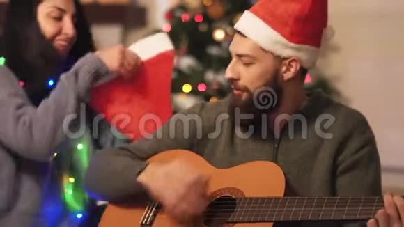 现代人坐在圣诞树附近的地板上弹吉他唱歌快乐的一对准备视频的预览图