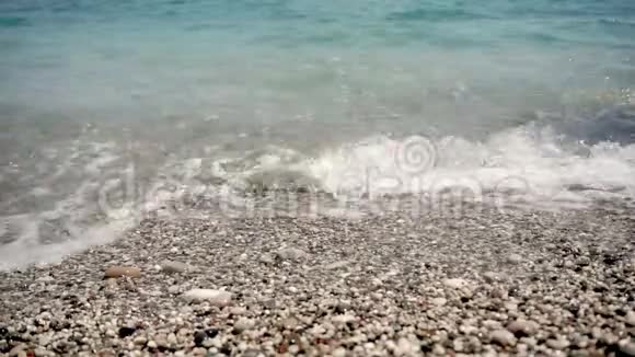 在斯劳莫女孩的腿用鹅卵石铺在沙滩上她的腿被小波浪和泡沫冲刷着视频的预览图
