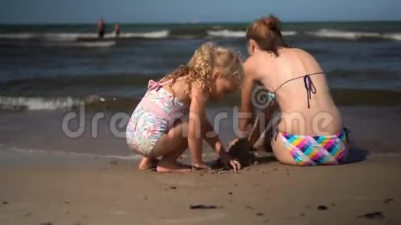 穿着泳衣的女儿和妈妈在海边建了一座潮湿的沙堡视频的预览图