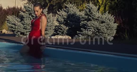穿红色衣服的性感年轻女子站在游泳池里在阳光下摆姿势4K视频的预览图