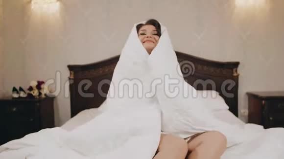 迷人的女孩裹着毯子坐在床上视频的预览图