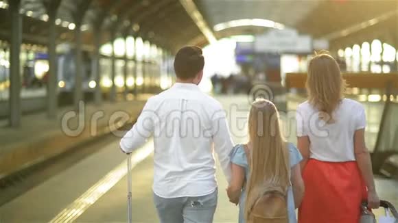 年轻的家庭带着可爱的女儿走在铁路站台上提着手提箱最佳旅行和度假概念视频的预览图