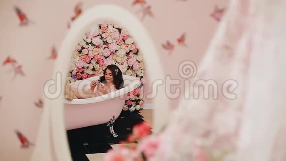 美丽的女孩躺在浴缸里手里拿着电话脸上的笑容有趣的镜头视频的预览图