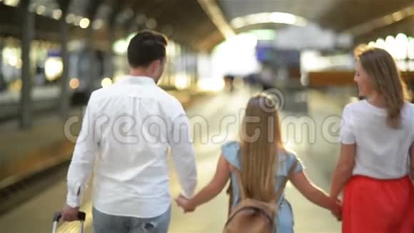 年轻的家庭带着可爱的女儿走在铁路站台上提着手提箱最佳旅行和度假概念视频的预览图