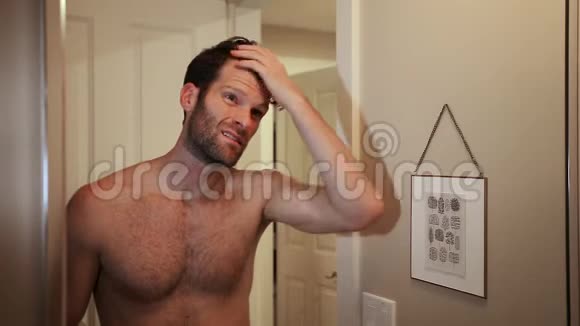 英俊的白种人年轻男子看着自己在浴室的镜子同时检查他的后退的发际线由于年龄视频的预览图