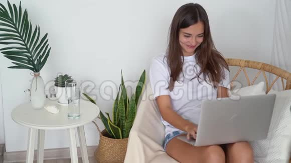 女孩笑了笑了坐在椅子上在笔记本电脑键盘上打字慢动作视频的预览图