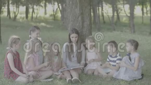 Vlog女青年作为教育家在公园为男孩和女孩读书视频的预览图