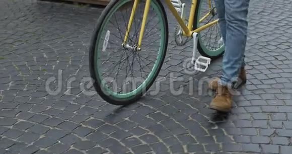 在现代黄薄轮胎自行车附近的旧石洞上行走的牛仔裤和休闲靴的特写镜头侧面视频的预览图