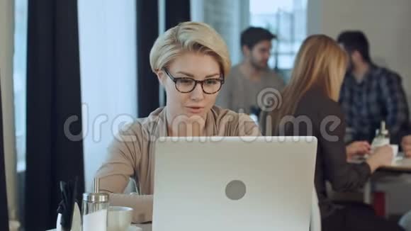 在咖啡厅休息时一个在笔记本电脑上工作的快乐女人视频的预览图