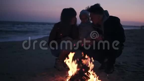 年轻的白种人一家人坐在篝火旁享受户外的亲密时光晚享受着亲密的生活视频的预览图