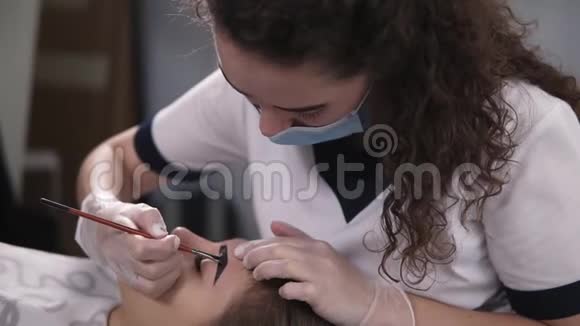 橱柜里的专业美容师用棕色染料轻轻地在年轻女子的眉毛上涂上颜料着色视频的预览图