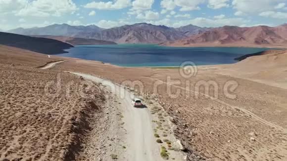 在4x4路的高空汽车沿着砾石小径驶向干旱山区的湖泊帕米尔公路丝绸之路视频的预览图
