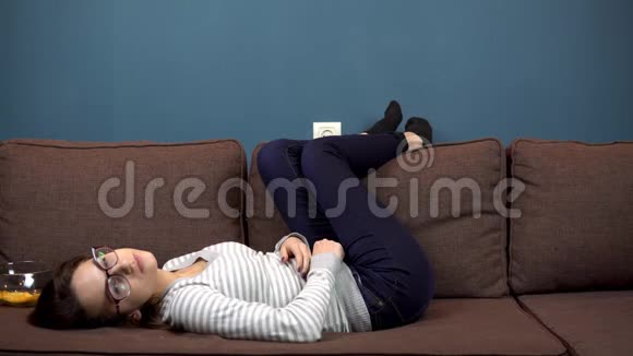 一个戴眼镜的年轻女人看电视躺在沙发上的女孩视频的预览图