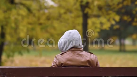 坐在公园长椅上的头罩里的无名男子正在看视频的预览图
