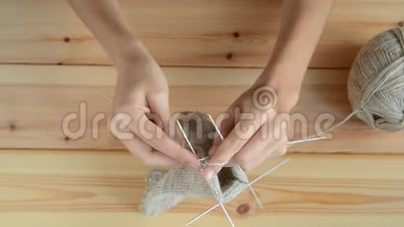 成年女孩在木桌背景上用灰色金属针和羊毛线编织视频的预览图