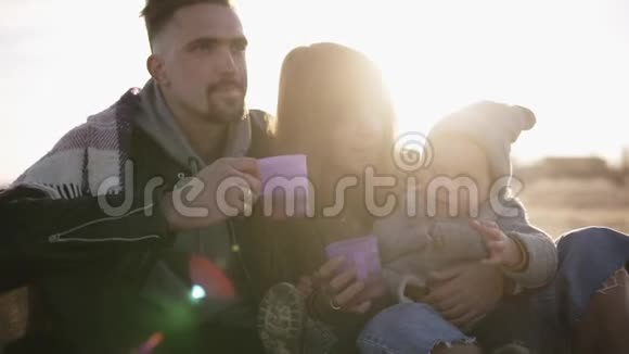 年轻时尚的家庭穿着休闲服坐在格子布上拥抱和享受在一起的时光喝酒视频的预览图