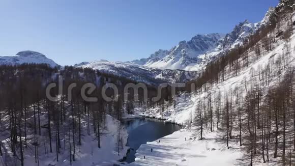 晴朗的冬日空中俯瞰阿尔卑斯湖露出雪山山谷欧洲阿尔卑斯山户外视频的预览图