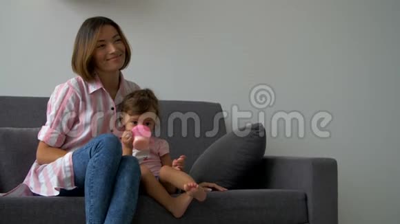 妈妈教小女儿用杯子喝水幸福美满的爱心家庭年轻母女笑坐在c视频的预览图
