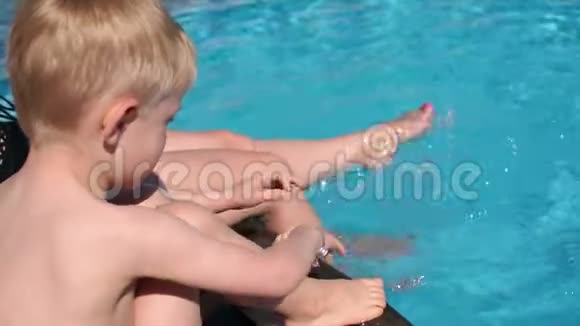 母亲和儿子在游泳池里玩耍他们坐在池边溅起水花视频的预览图