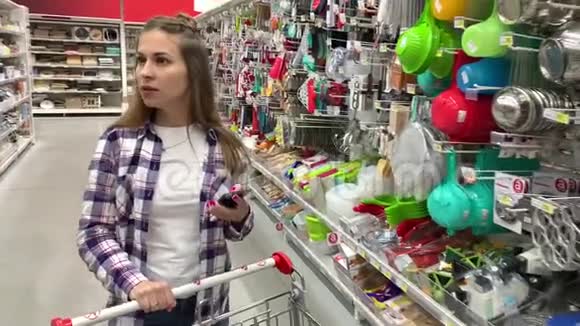 一个年轻的家庭主妇带着手推车在超市里走来走去她在看电话里的购物清单4K慢Mo视频的预览图