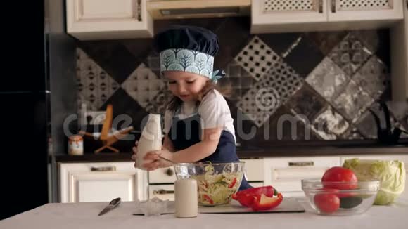 可爱的三岁女孩戴着帽子和围裙在厨房做饭视频的预览图