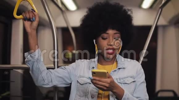 戴着耳机听音乐唱歌和在公共场合跳搞笑舞的非洲裔美国年轻妇女的画像视频的预览图