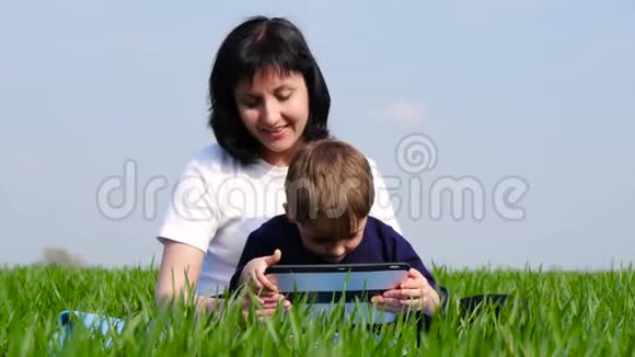 母子俩正看着碑屏坐在公园的绿草上母亲和儿童的经历视频的预览图