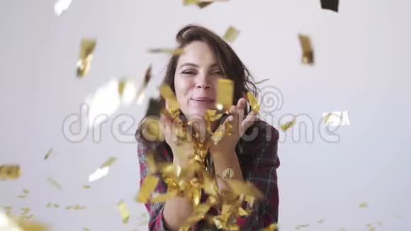 美丽的美女在白色背景上吹着金色的五彩纸屑视频的预览图
