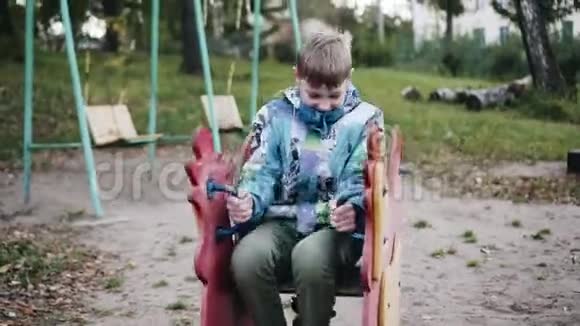 这个男孩坐在弹簧上的木椅上摇摆有趣的时刻视频的预览图