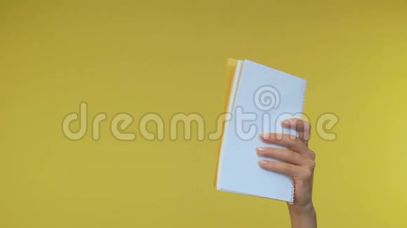 女性手在一个孤立的黄色背景上拿着一个笔记本读笔记4K视频的预览图
