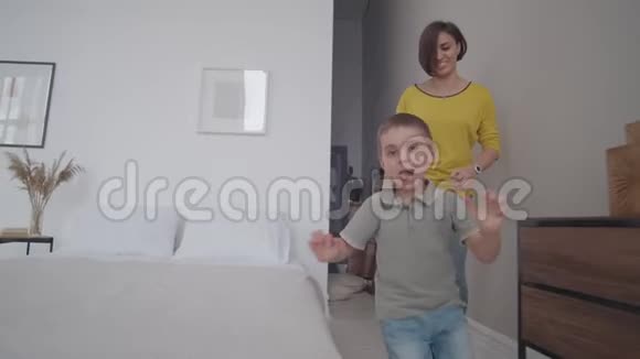 妈妈和儿子在白色的室内玩追赶游戏玩得很开心和你的孩子在房子里跑来跑去玩躲猫猫视频的预览图