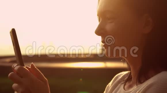 女人在背景下的日落时分在她的手机上打字视频的预览图