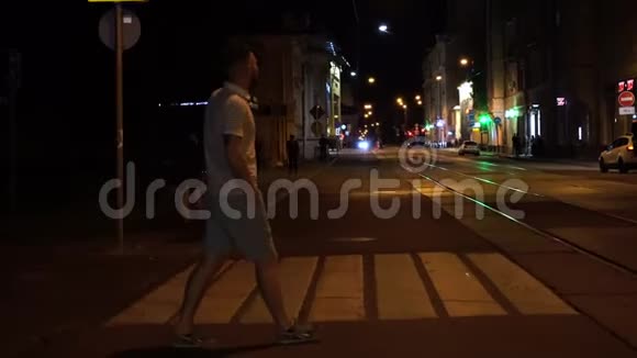 穿着条纹马球和绿色短裤的长胡子男人晚上在人行横道上穿过马路视频的预览图