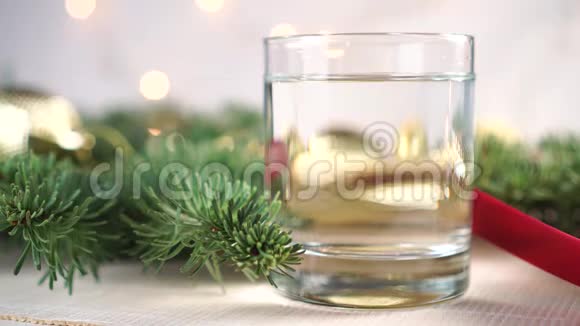一个杯子桌子上放着干净的水上面有活云杉树枝还有闪烁的圣诞装饰视频的预览图