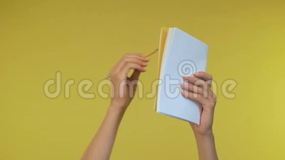 女性手在一个孤立的黄色背景上用铅笔在笔记本上做笔记黄色背景4K视频的预览图