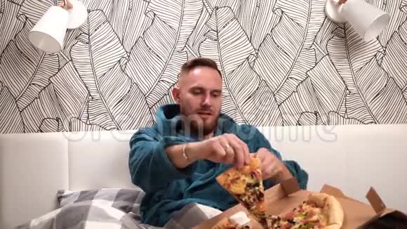 床上穿着绿色浴袍的大胡子男人在卧室里吃披萨尽情享受视频的预览图