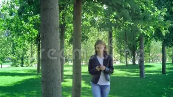 前面看到一个困惑的女人走路检查智能手机内容然后停止看相机在公园一个年轻人视频的预览图