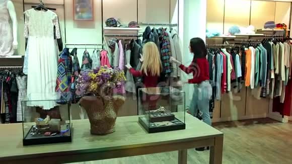 两个年轻时尚的女人在一家现代商店里选择秋冬大衣视频的预览图