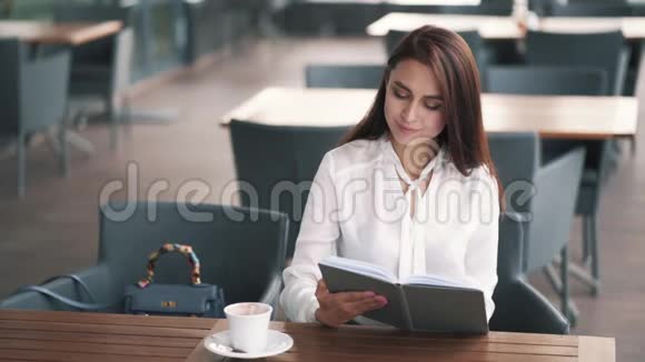 女商人坐在咖啡馆里喝着咖啡看着她的日记慢动作视频的预览图