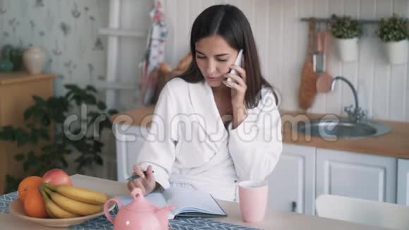 女人打电话写日记在厨房喝茶慢动作视频的预览图