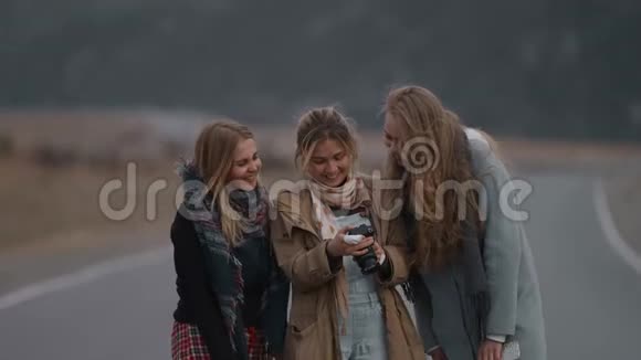 三个年轻漂亮的女朋友旅行者在户外看着镜头里的照片在路上笑着金发朋友看ph视频的预览图