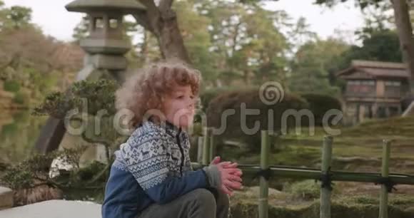 小男孩坐在日本花园池塘旁边的桥尾深呼吸视频的预览图