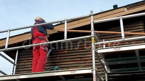 在屋顶屋檐上安装新木板的脚手架上的工人视频的预览图