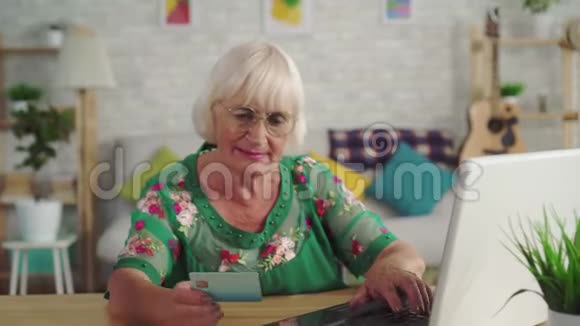 戴眼镜的白发老年妇女持有银行卡使用笔记本电脑视频的预览图