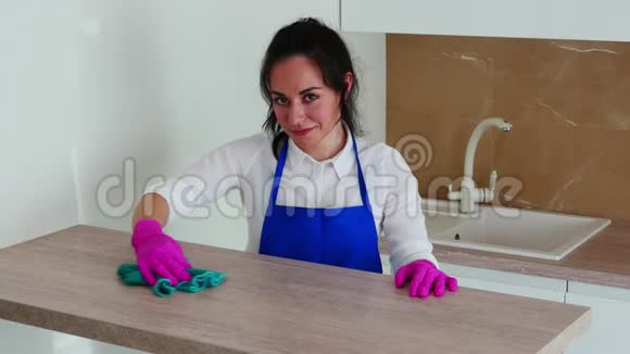 一个黑发女孩正在清洁和微笑的相机搓一桌轻木用于清洁的粉红色手套视频的预览图