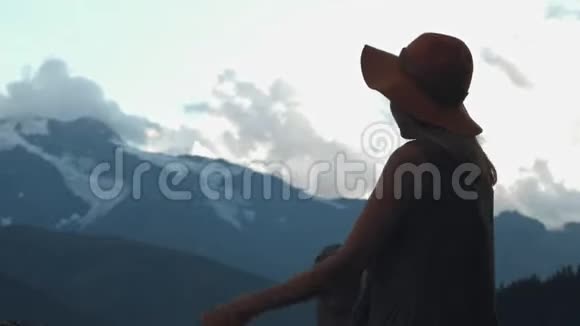 带着帽子的时髦女孩的后景带着去山的旅程兴奋不已快乐的年轻女人四处游荡望着阿尔卑斯山的山峰视频的预览图