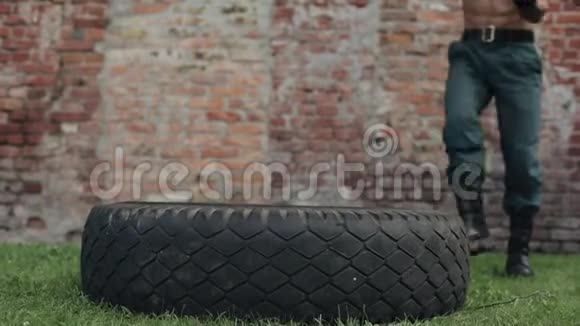 强壮的肌肉赤膊的年轻人用大锤打轮胎背景上的红砖建筑视频的预览图