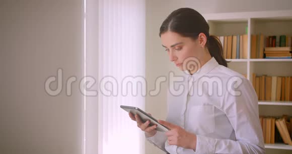 年轻迷人的高加索女商人用平板电脑站在办公室书架上摆着一幅特写肖像视频的预览图