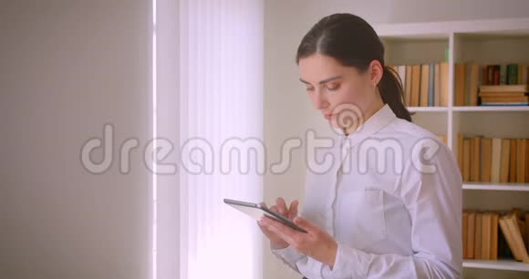 年轻的白种人女商人用平板电脑看着相机微笑站在办公室的特写照片视频的预览图