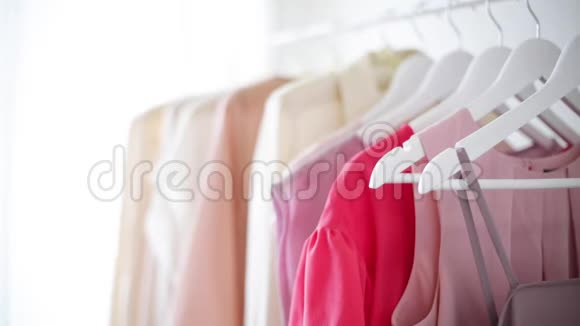 白色衣架上穿粉色米色和奶油色的女式服装特写镜头一个女人拿起一件衬衫溅起视频的预览图